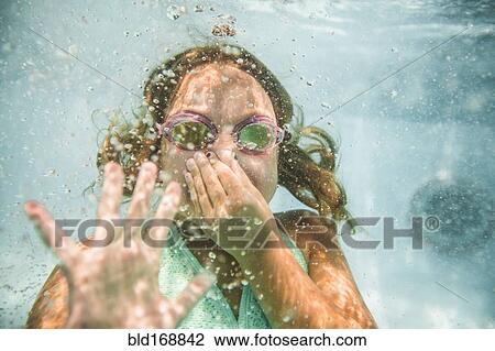 Stock Image - Caucasian girl holding nose underwater in swimming pool. Fotosearch