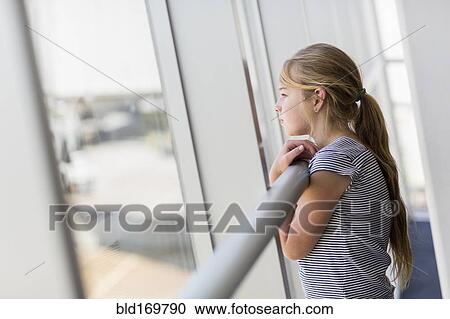 Stock Image - Caucasian girl looking out airport window. Fotosearch