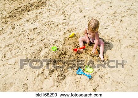 Stock Image - Caucasian girl playing in sand on beach. Fotosearch