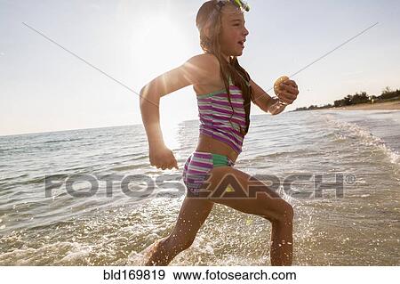 Stock Photo - Caucasian girl running in ocean waves on beach. Fotosearch