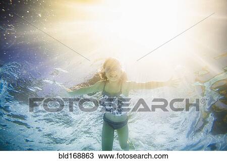 Stock Image - Caucasian girl swimming underwater in swimming pool. Fotosearch