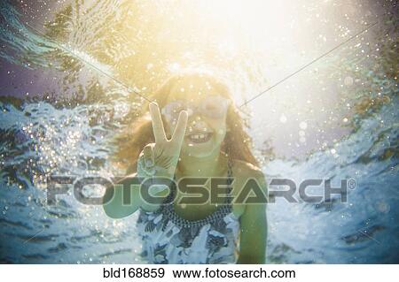 Stock Photo - Caucasian girl swimming underwater gesturing peace sign. Fotosearch