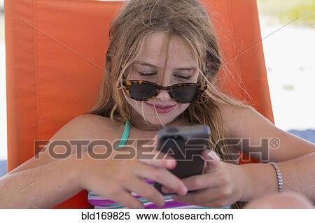 Stock Photography - Caucasian girl using cell phone on beach. Fotosearch