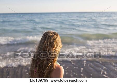 Stock Photo - Caucasian girl watching waves on beach. Fotosearch