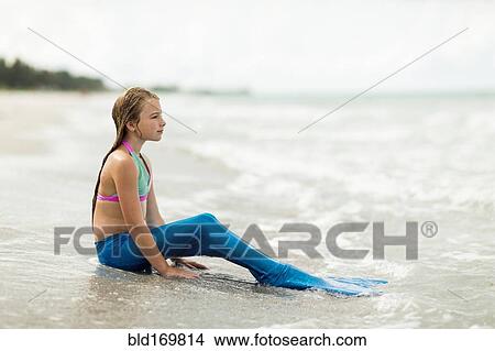 Picture - Caucasian girl wearing mermaid fin on beach. Fotosearch