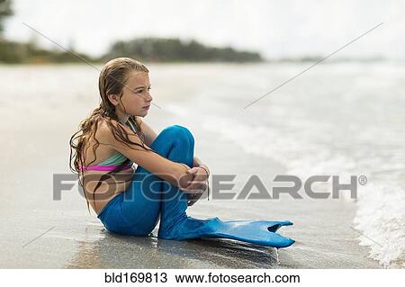 Stock Image - Caucasian girl wearing mermaid fin on beach. Fotosearch