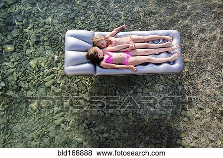Stock Photo - Caucasian girls floating on raft in lake. Fotosearch