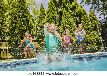 Stock Image - Caucasian girls jumping into swimming pool. Fotosearch