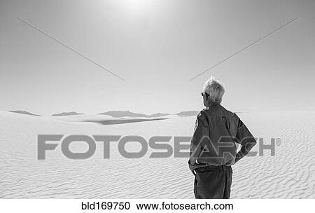 Stock Image - Caucasian man admiring desert sand dunes. Fotosearch
