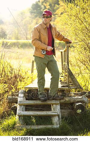 Stock Image - Caucasian man holding fishing pole on steps. Fotosearch