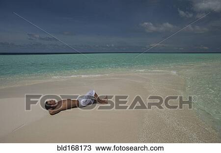 Stock Image - Caucasian man laying on beach. Fotosearch