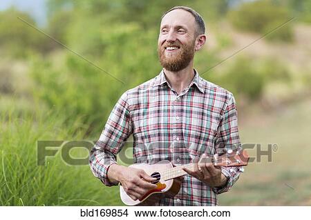 Picture - Caucasian man playing ukulele outdoors. Fotosearch