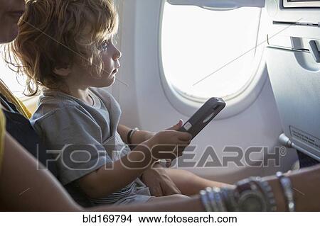 Picture - Caucasian mother and baby son using cell phone on airplane. Fotosearch
