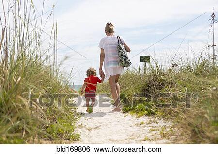 Stock Photograph - Caucasian mother and baby son walking on beach. Fotosearch