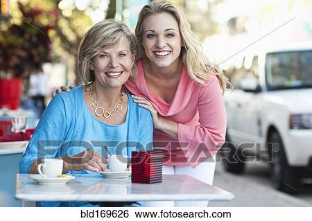Stock Photograph - Caucasian mother and daughter drinking coffee at sidewalk cafe. Fotosearch