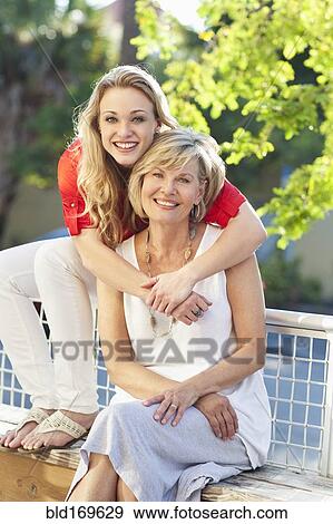 Stock Photo - Caucasian mother and daughter hugging on bench. Fotosearch
