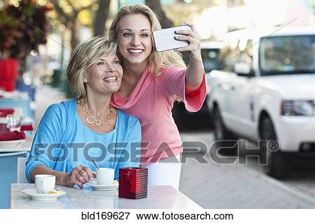 Stock Photo - Caucasian mother and daughter taking selfie at sidewalk cafe. Fotosearch