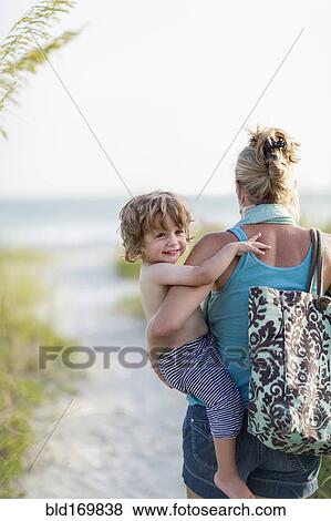 Stock Photo - Caucasian mother carrying baby son on beach. Fotosearch
