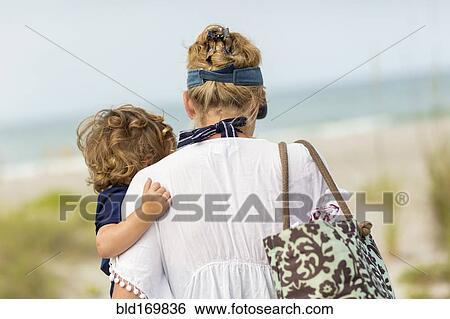Stock Photograph - Caucasian mother carrying baby son on beach. Fotosearch