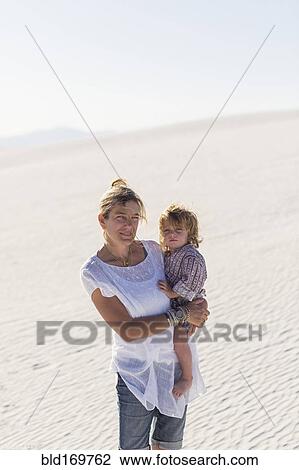 Stock Image - Caucasian mother holding son on desert sand dune. Fotosearch