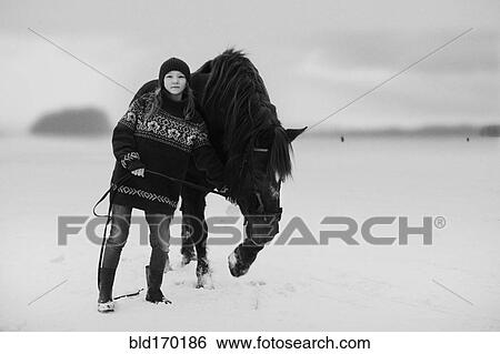 Stock Photograph - Caucasian teenage girl leading horse in snowy field. Fotosearch