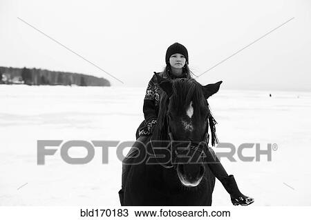 Stock Image - Caucasian teenage girl riding horse in snowy field. Fotosearch