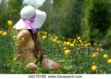 Stock Photo - Caucasian teenage girl sitting in field with flowers. Fotosearch