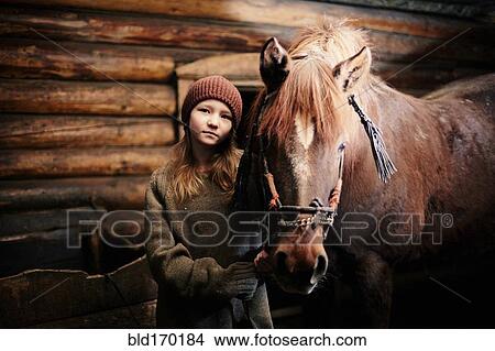 Picture - Caucasian teenage girl standing with horse in barn. Fotosearch