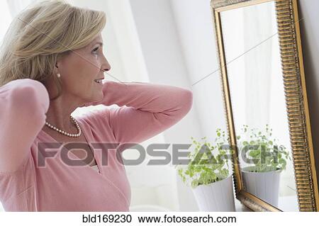 Stock Image - Caucasian woman admiring herself in mirror. Fotosearch