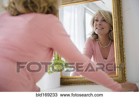 Stock Image - Caucasian woman admiring herself in mirror. Fotosearch