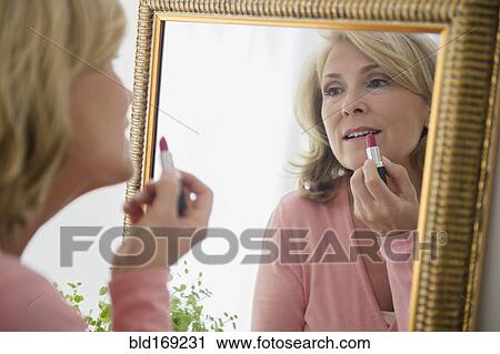 Stock Image - Caucasian woman applying lipstick in mirror. Fotosearch