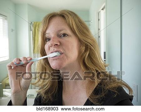 Stock Image - Caucasian woman brushing her teeth in bathroom. Fotosearch