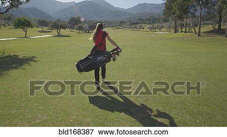 Stock Photo - Caucasian woman carrying golf bag on course. Fotosearch