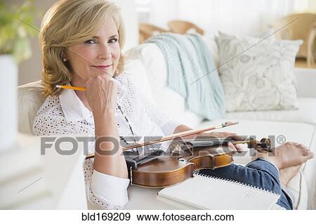 Stock Photo - Caucasian woman holding violin on sofa. Fotosearch