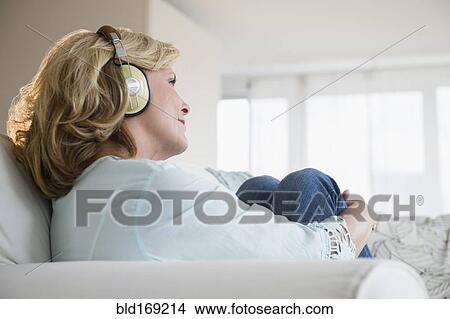 Picture - Caucasian woman listening to headphones on sofa. Fotosearch