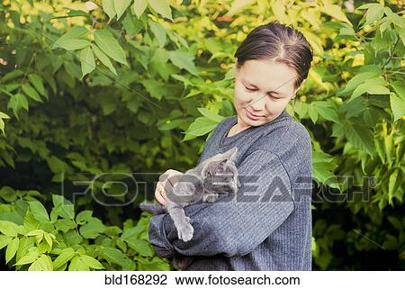 Stock Image - Caucasian woman petting cat in garden. Fotosearch
