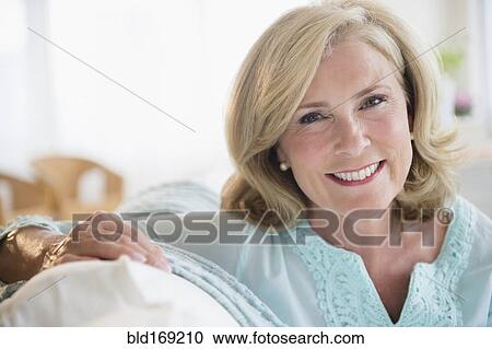 Stock Image - Caucasian woman smiling on sofa. Fotosearch