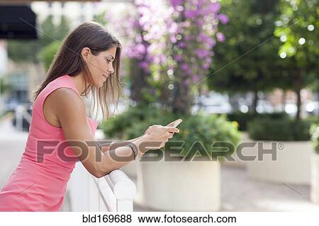 Stock Photo - Caucasian woman using cell phone at fence. Fotosearch