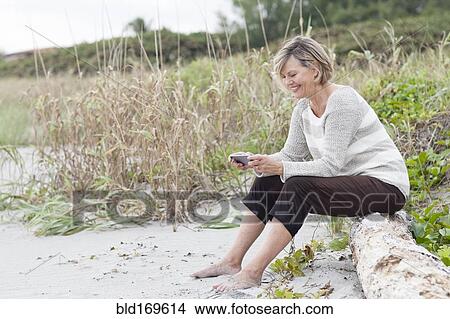 Picture - Caucasian woman using cell phone on beach. Fotosearch