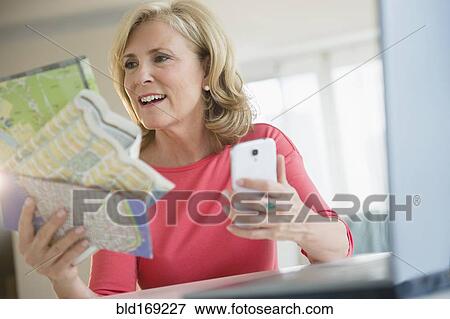 Stock Photo - Caucasian woman using roadmap and cell phone to plan trip. Fotosearch