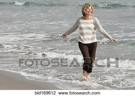 Stock Image - Caucasian woman wading on beach. Fotosearch