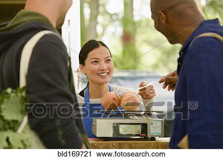 Stock Image - Clerk helping customers at farmers market. Fotosearch