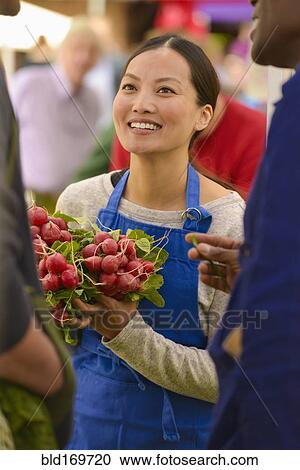 Stock Image - Clerk holding produce at farmers market. Fotosearch