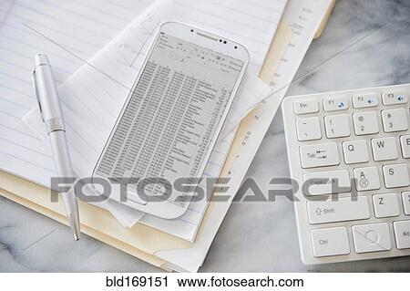 Stock Image - Close up of computer keyboard, files and cell phone on office desk. Fotosearch