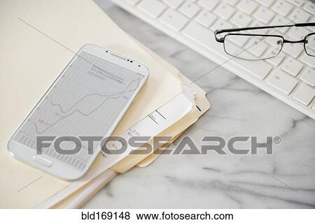 Stock Photo - Close up of computer keyboard, files, cell phone and eyeglasses on office desk. Fotosearch