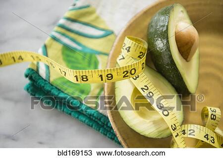 Stock Image - Close up of halved avocado, measuring tape and napkin on plate. Fotosearch