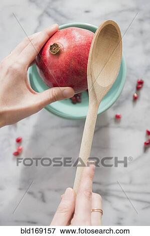 Stock Photo - Close up of hands cracking pomegranate with spoon. Fotosearch