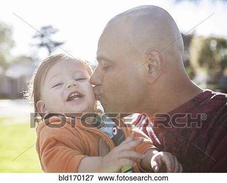 Stock Photo - Close up of Hispanic father kissing cheek of son outdoors. Fotosearch
