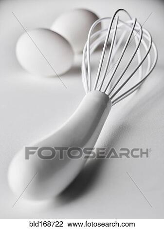 Stock Image - Close up of white whisk and eggs. Fotosearch