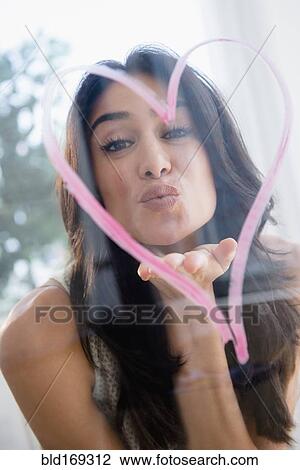 Stock Image - Close up of woman blowing a kiss through heart. Fotosearch